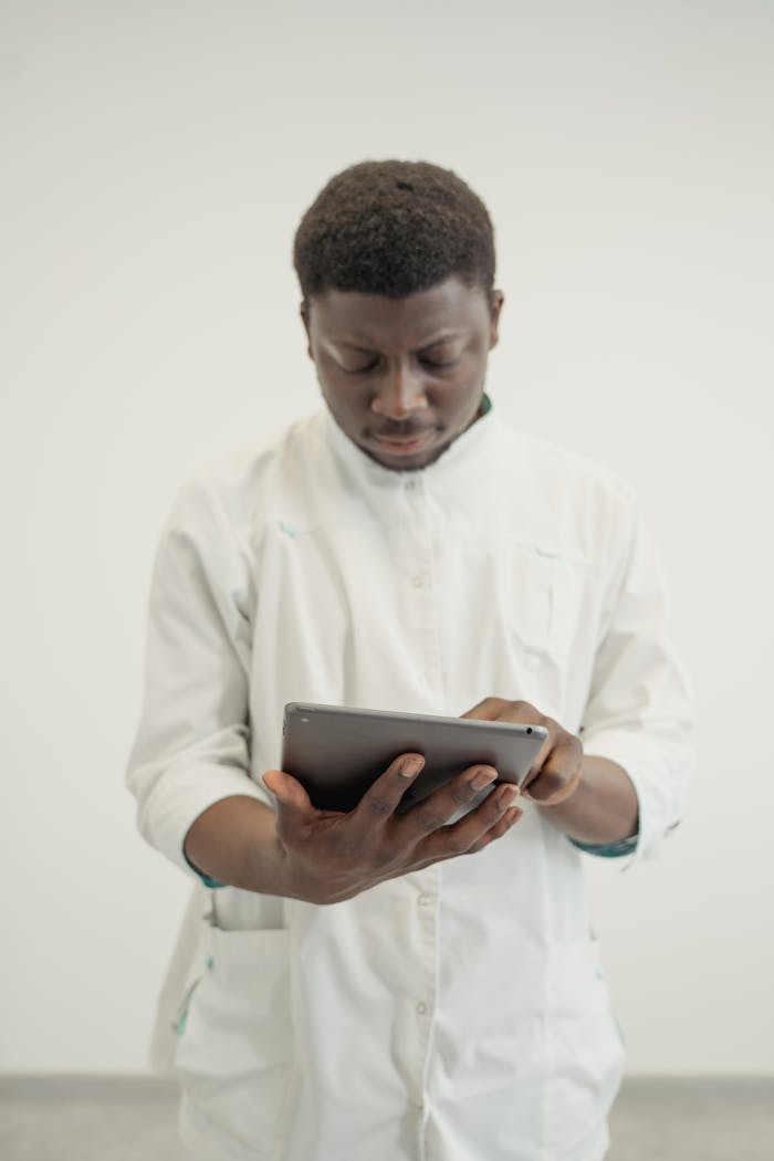 A focused male medical professional uses a tablet in a clinical setting.